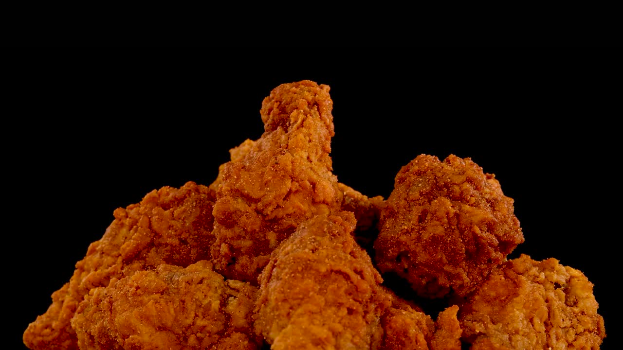 Crispy fried chicken wings and nuggets rotate and zoom in slow motion against a black background, with dramatic lighting highlighting golden, spicy breading