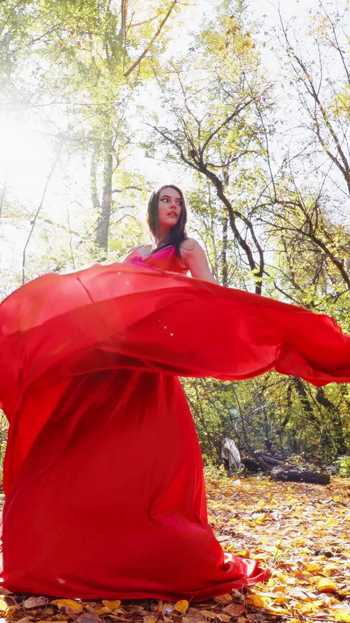 Captivating Elegance: A Woman in a Flowing Red Dress Twirls Amidst the Golden Autumn Leaves, Embracing the Beauty of Nature and Fashion in the Enchanting Forest Light