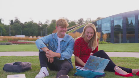 Group-Of-University-Or-College-Students-Sit-On-Grass-Outdoors-On-Campus-Talking-And-Working