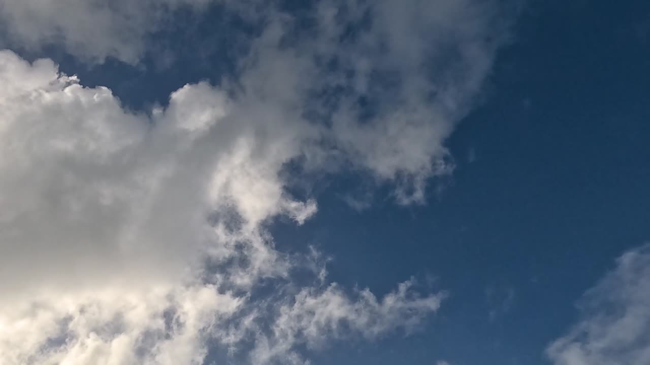 White fluffy clouds drift across a vibrant blue sky with a hint of greenery.