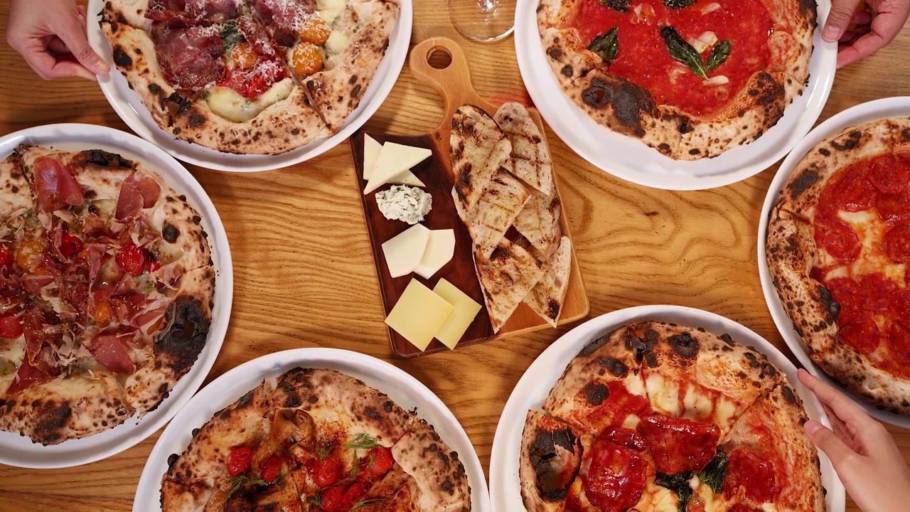 Ellerin çeşitli Napoli pizzalarını ve şarküteri tabağını bir masaya yerleştirdiği kuşbakışı görünüm