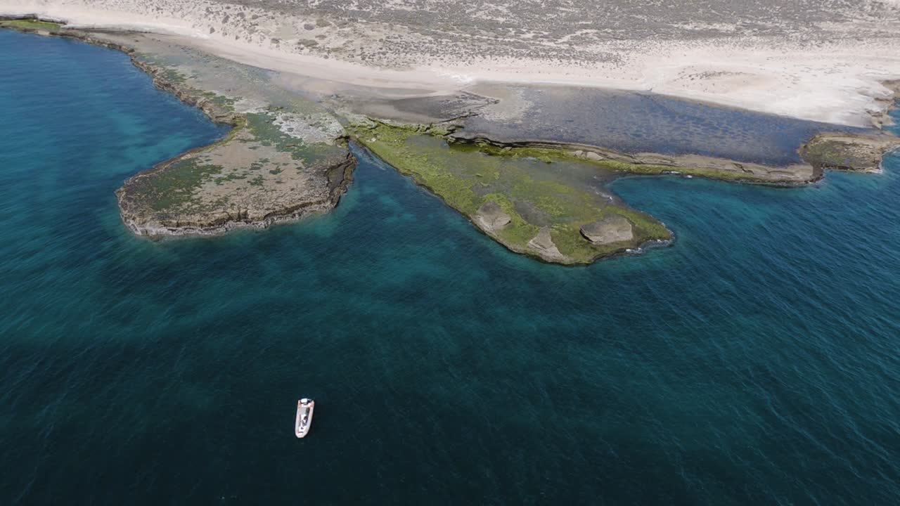 bote zodiac flotando en el mar turquesa cerca de la costa patagónica - toma aérea de pedestal