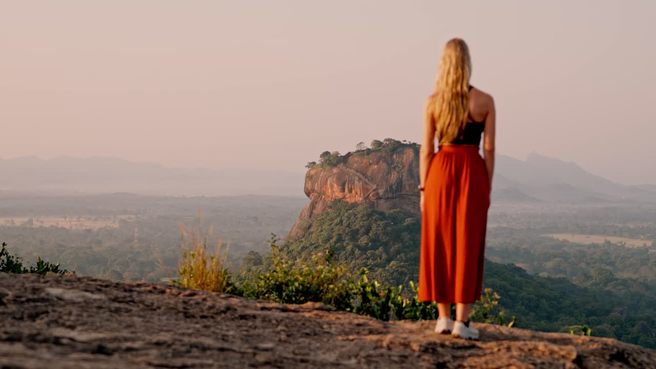 A woman admires the majestic Sigiriya Rock as the sun rises over the Sri Lankan jungle. A peaceful and iconic moment in nature, perfect for travel and cultural themes.