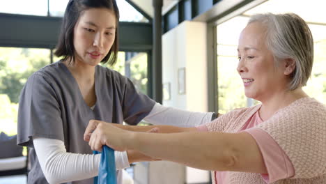 helping senior asian woman with resistance band, young physiotherapist providing home care