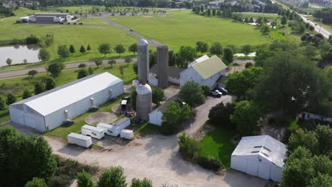 Aerial-establishing-dolly-over-farmhouse,-silo,-and-long-shed-next-to-open-fields