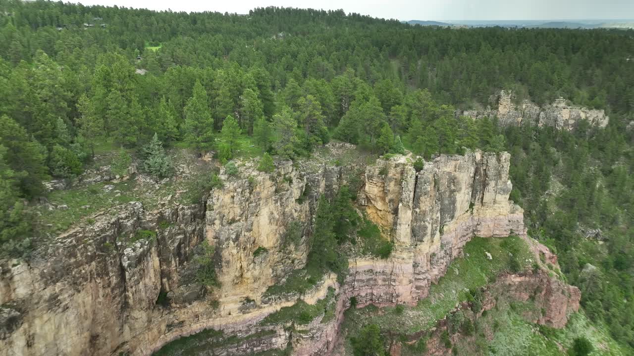 Drone shot orbiting around a cliff edge in a forested area