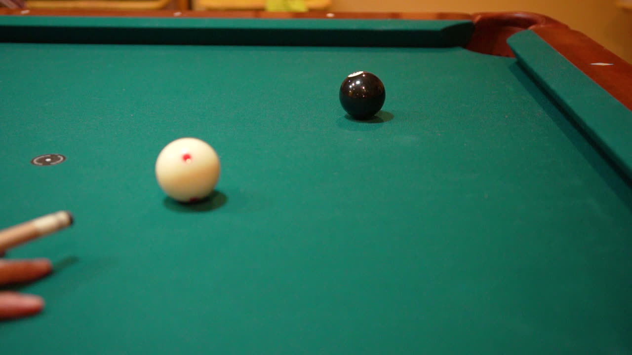Slow motion beelden van een biljarter die de massieve zwarte 8-ball in de hoekpocket schiet op een pooltafel met groen laken, waarbij de witte bal met een stun-stoot op zijn plaats blijft na oefenstoten met de keu - close-up