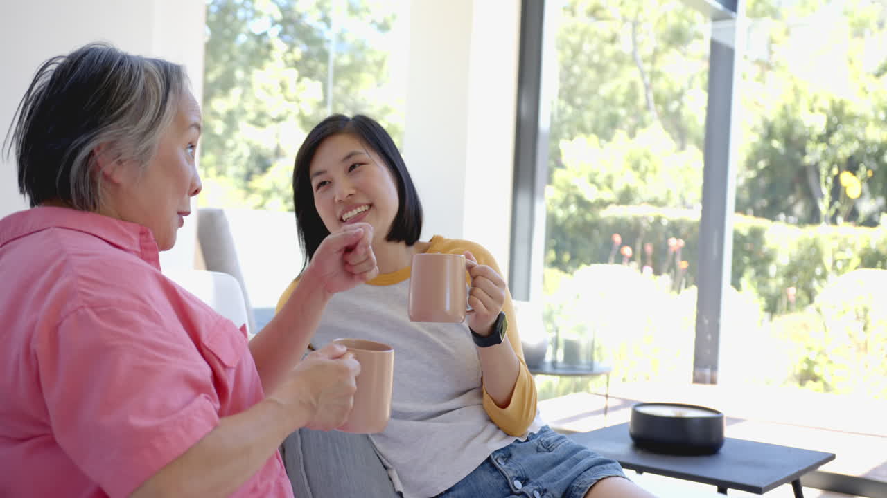 Smiling women enjoying coffee together, relaxing on couch in bright living room