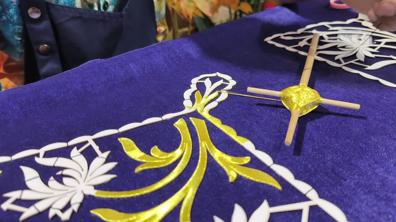 Seorang perajin terampil menampilkan sulaman Tekat Melayu tradisional. Ia dengan cermat menyulam benang emas di atas kain beludru mewah. Kerajinan kuno yang langka ini mewakili bentuk seni warisan yang semakin menghilang.