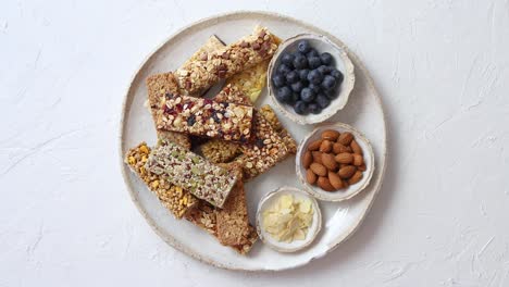 Mixed-composition-of-energy-nutrition-bar--granola-on-ceramic-plate-over-white-background