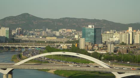 Vista-Superior-Del-Tráfico-De-Automóviles-En-El-Puente-Eungbonggyo-Y-La-Autopista-De-Seúl-Cerca-Del-Río-Han-Desde-Un-Punto-De-Vista-Alto,-Muchos-Edificios-Y-Colinas-En-El-Fondo