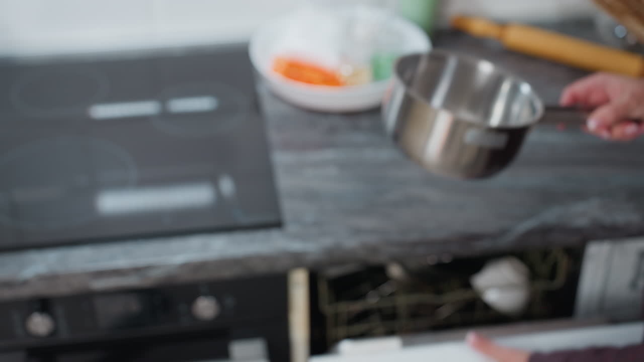 задний вид женщина, берущая горшок из шкафа, помещающая его на гладкую электрическую плиту, поворачивающую плиту на современную кухню с посудой для выпечки и цифровыми устройствами управления