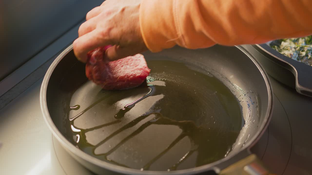 Cooking two vegan burgers and two steaks in a pan with olive oil