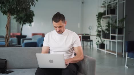 young-handsome-man-works-on-a-laptop-in-the-office-and-then-finishes-his-work-with-relief