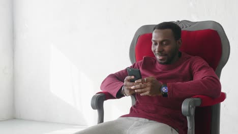 man sitting in red chair using smartphone