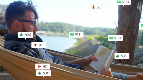 man reclining in lakeside hammock reading book, displaying animated social media marketing icons