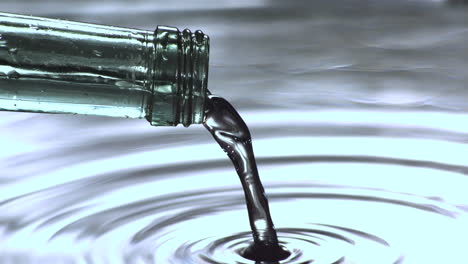 water pouring from glass bottle into water close up