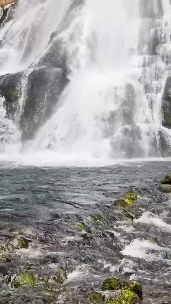 Vista dal basso dello sbocco della cascata di Golling, con acqua spumeggiante che scorre su pietre muschiose mentre la cascata principale si getta nella pozza retrostante.
