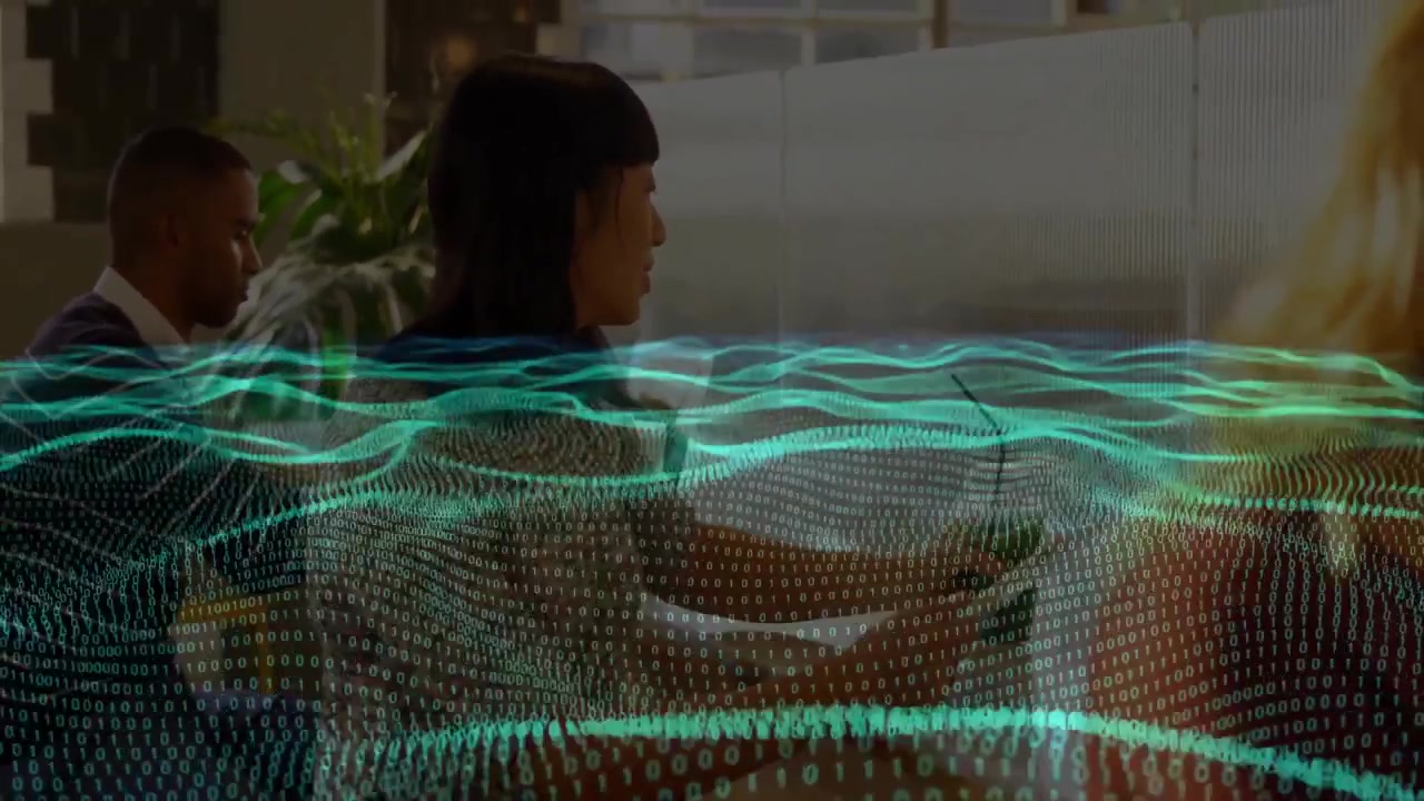 Asian woman in tech office glancing at keyboard and sipping drink while green data wave pulsing