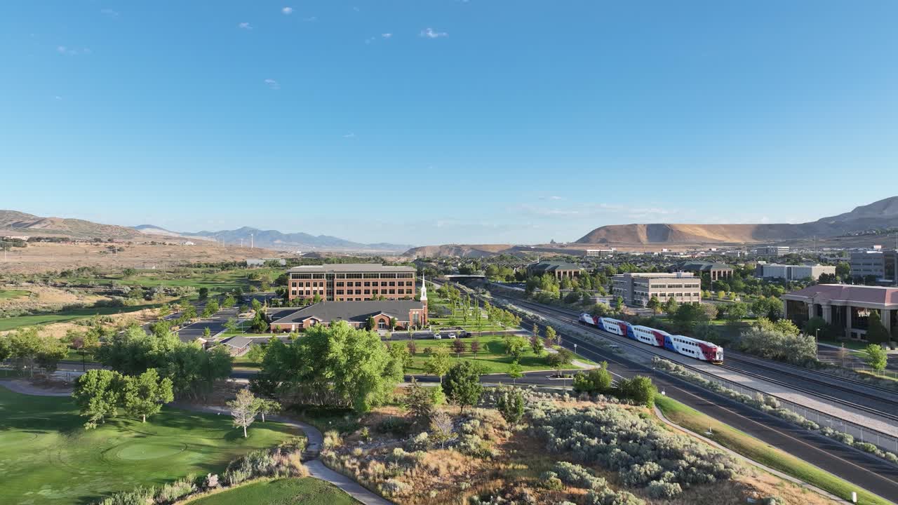 Southbound FrontRunner commuter train pulling into the Lehi Station on a sunny, picturesque morning - pullback aerial reveal