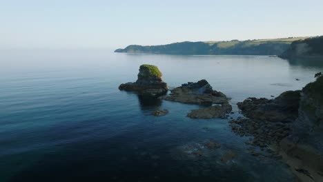 isolated sea cliff in calm water with camera flight towards revealing larger coastline. charlestown, cornwall, uk.