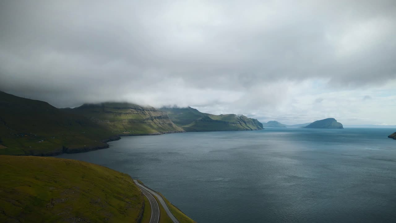 페로 제도 의 비비크 의 경치적 인 풍경, 거친 해안 절벽, 평온 한 푸른 물, 그리고 기분 좋지 않은 구름이 가득 찬 하늘, 울창 한 초록색 지형 에 사라지는 휘어지는 도로