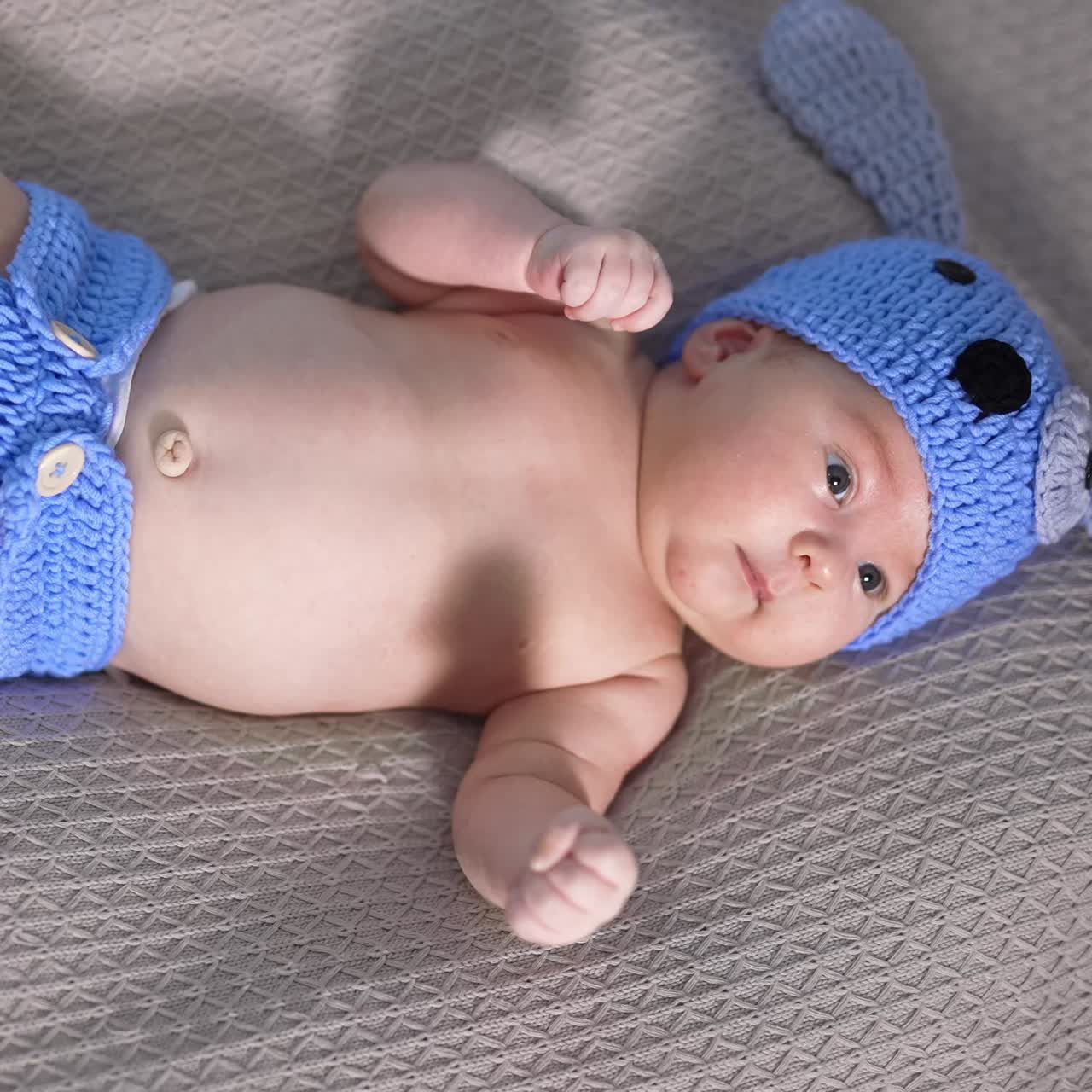 Tiny boy in a blue knitted hat and diaper lies on his back. Funny puppy costume for a small baby. View from above
