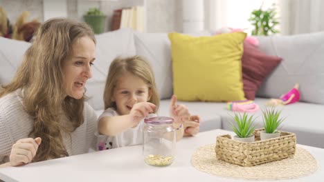 the little girl puts gold in the piggy bank with her mother.