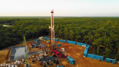 cinematic 4k drone footage of onshore drilling rig equipment structure for oil exploration and exploitation in the middle of jungle surrounded by palm oil trees during sunset and high oil price