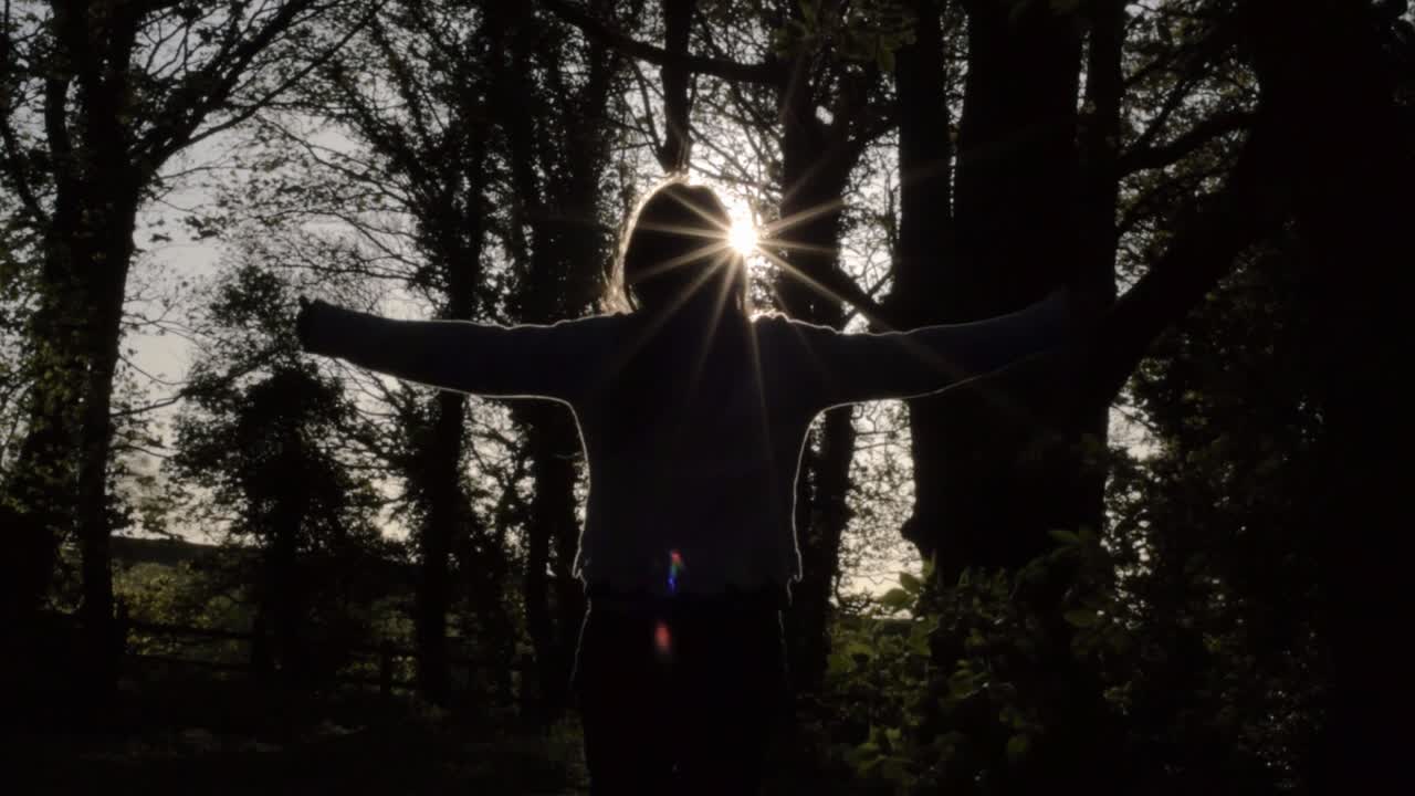 Woman stretching in woodland with lens flare at sunset medium