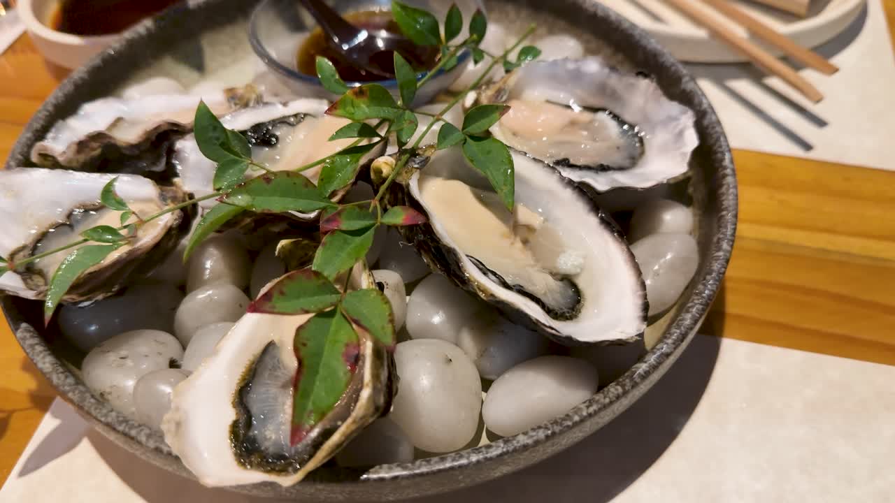 Käsi puristaa sitruunamehua tuoreille raaoille ostereille, jotka tarjoillaan ravintolassa jään päällä.