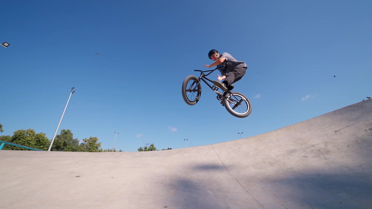 Giovane uomo in bici BMX che salta da una rampa di cemento in uno skatepark.