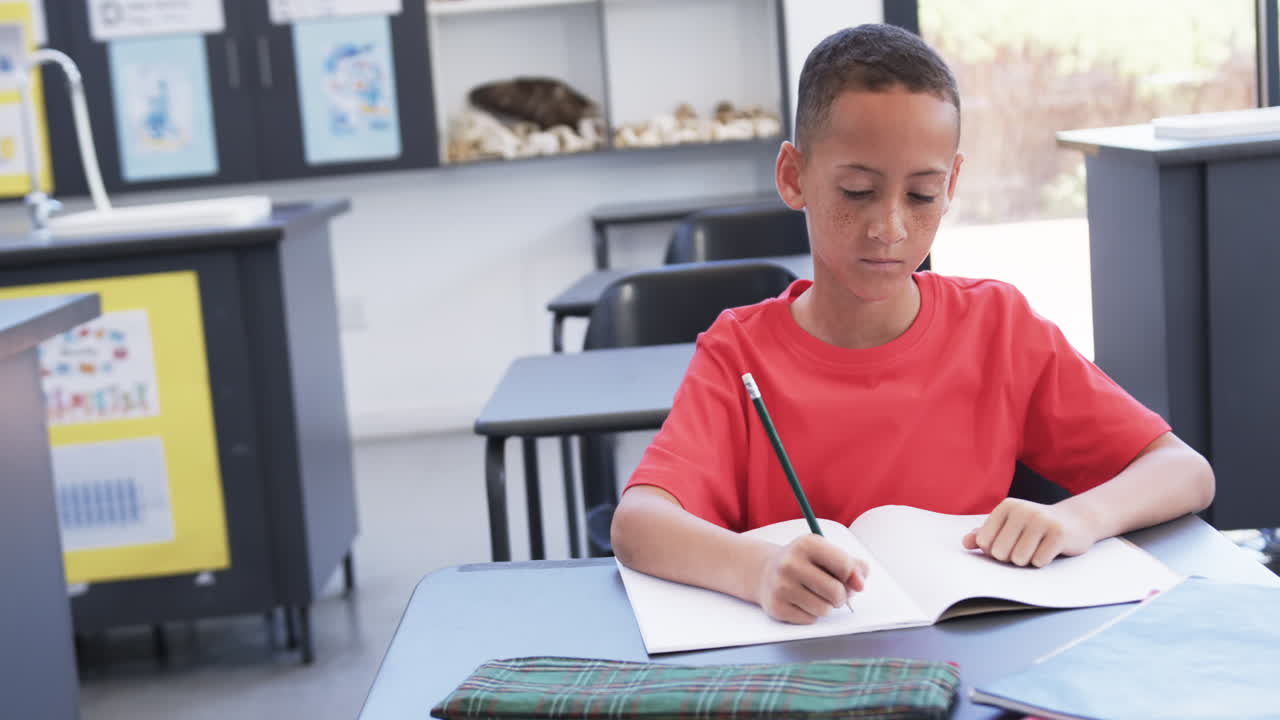 A young African American student writes intently in classroom, copy space