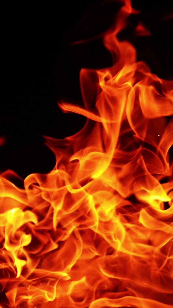 Grande falò acceso isolato sullo sfondo nero. Fiamme arancioni ardenti che si alzano. Primo piano. Video verticale