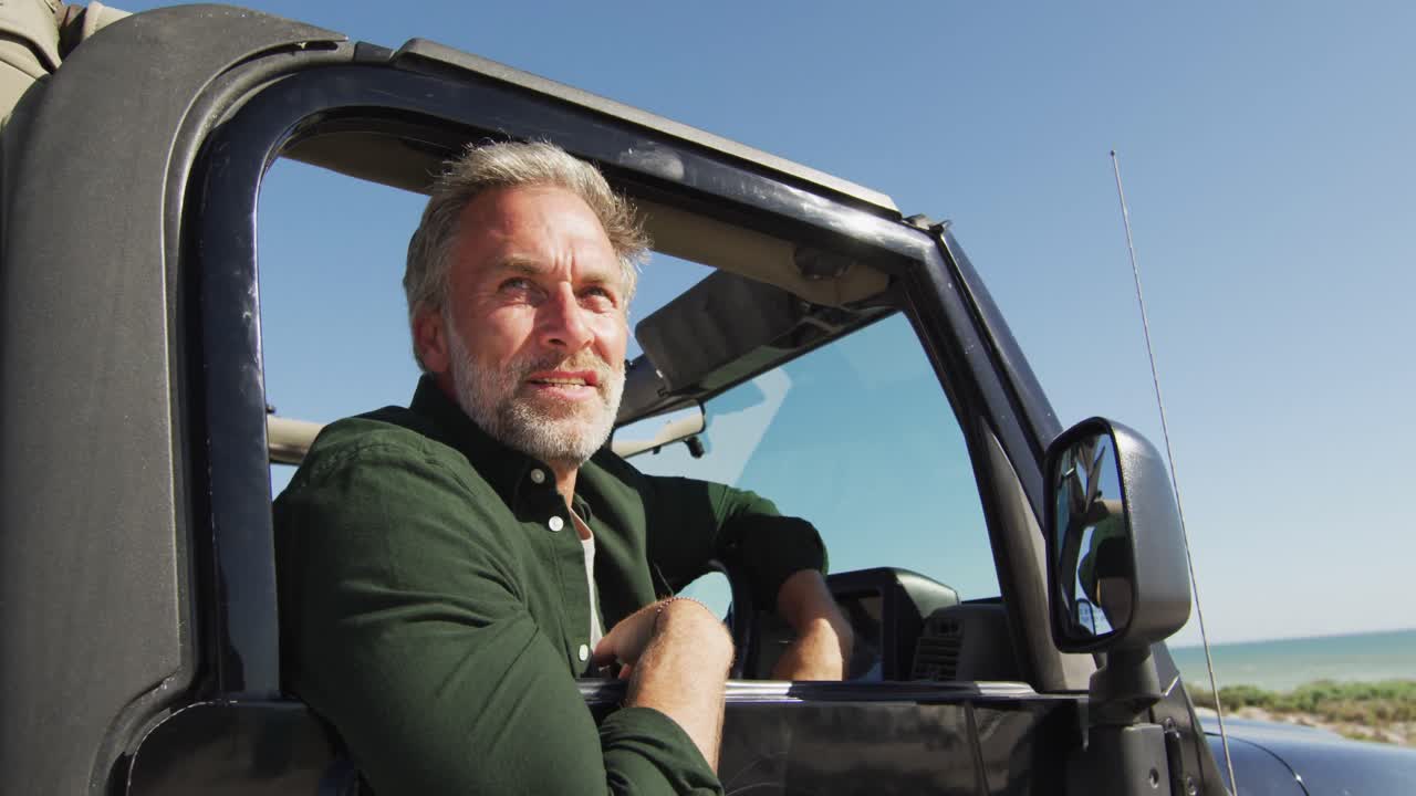 Glücklicher kaukasischer Mann im Auto bewundert die Aussicht an einem sonnigen Tag am Strand.