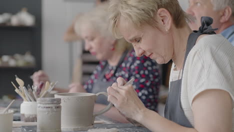 a group of elderly people at a master class in pottery together sculpt and cut a drawing on cups of clay for the manufacture of ceramic dishes