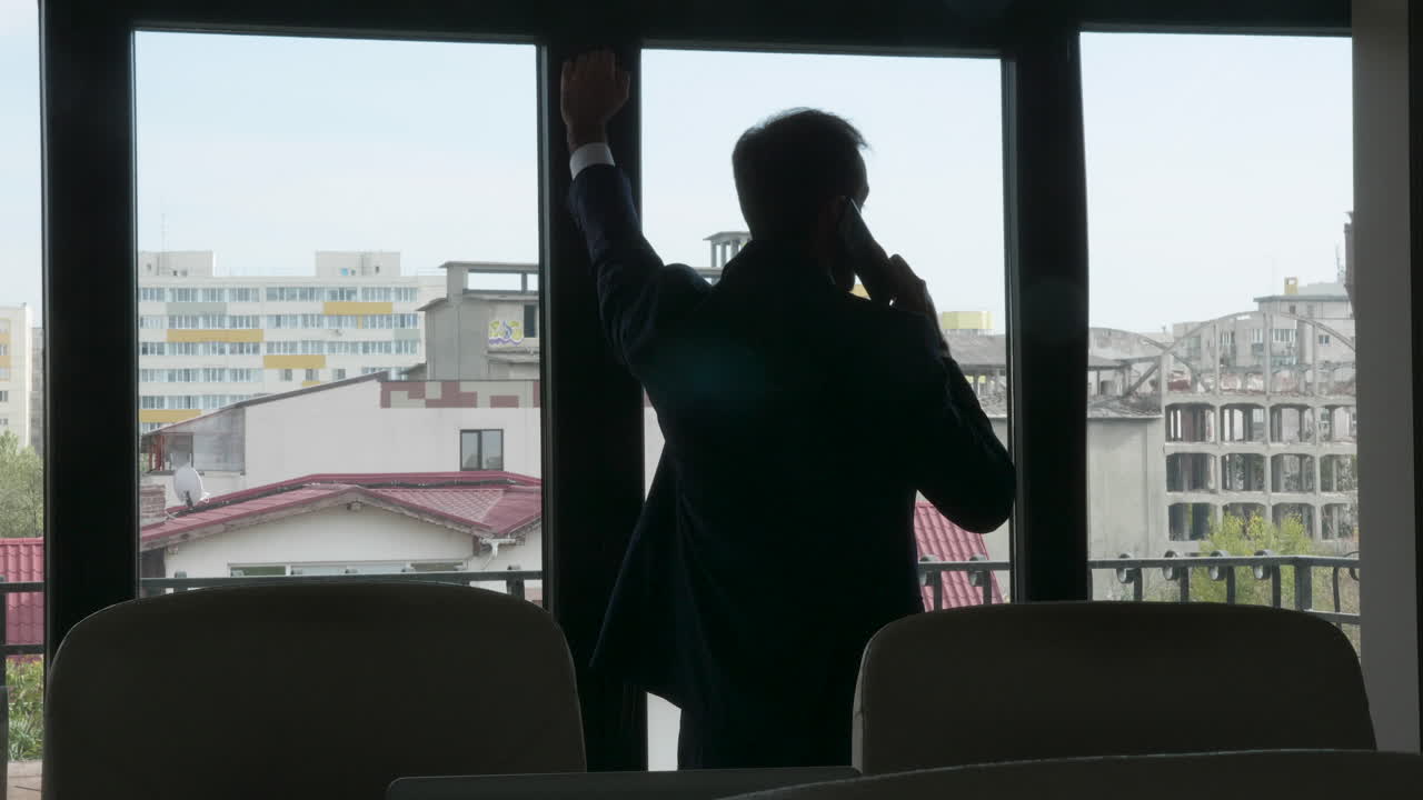 Silhouette of a man in a suit talking on the phone by a window