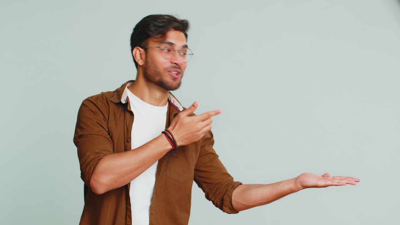 joven mostrando los pulgares hacia arriba y apuntando a la derecha en el espacio en blanco lugar para su logotipo de publicidad