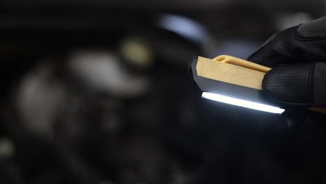 Slow-motion-shot-of-a-mechanic-using-a-small-light-to-look-in-the-engine-bay