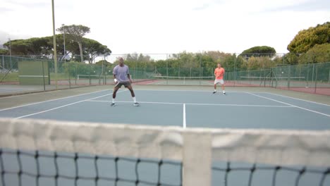 two diverse male friends playing doubles returning ball over net at outdoor court in slow motion