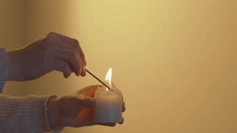 Candle-being-lit-in-front-of-a-plain-yellow-background