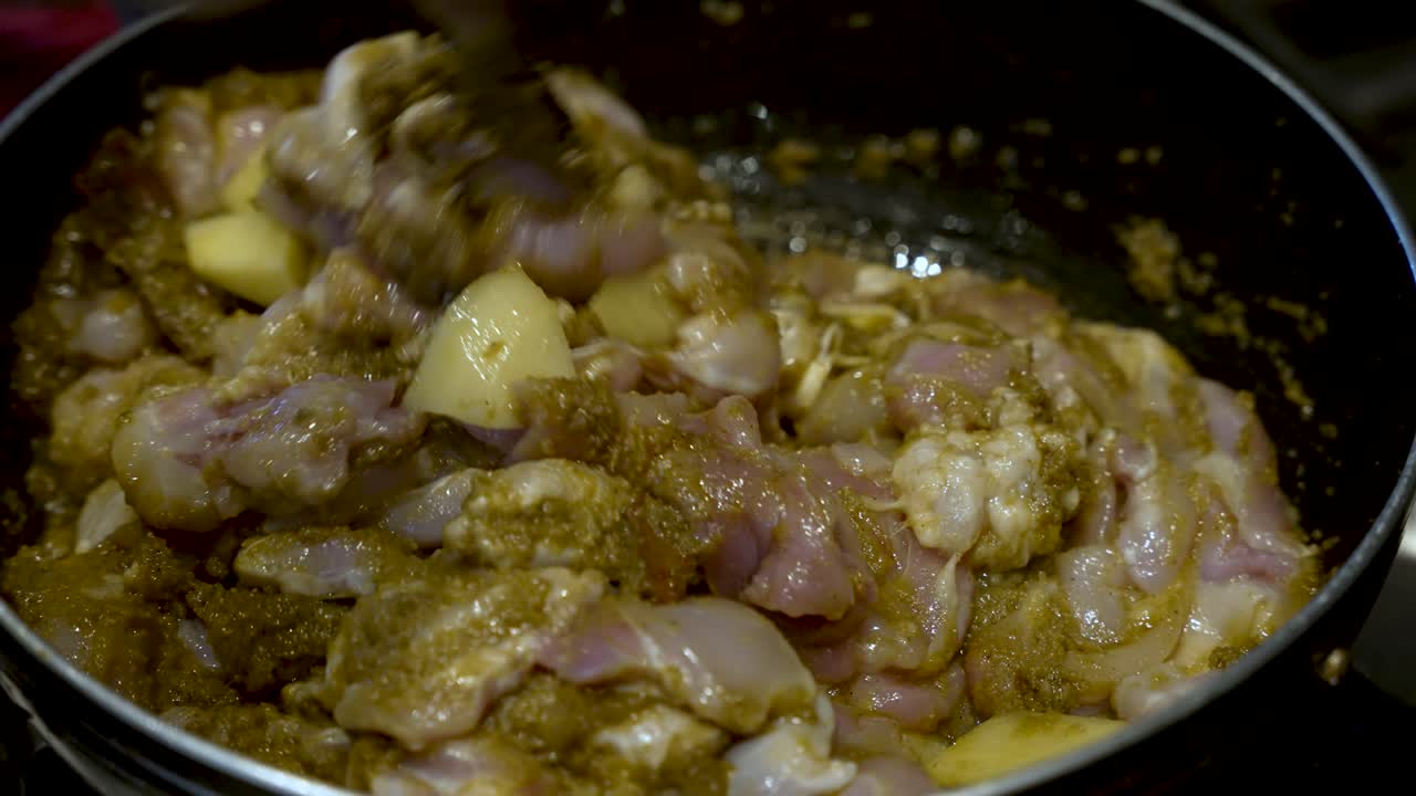 agitar pollo y curry de patatas en una sartén, escena de cocina en casa, iluminación cálida de la cocina