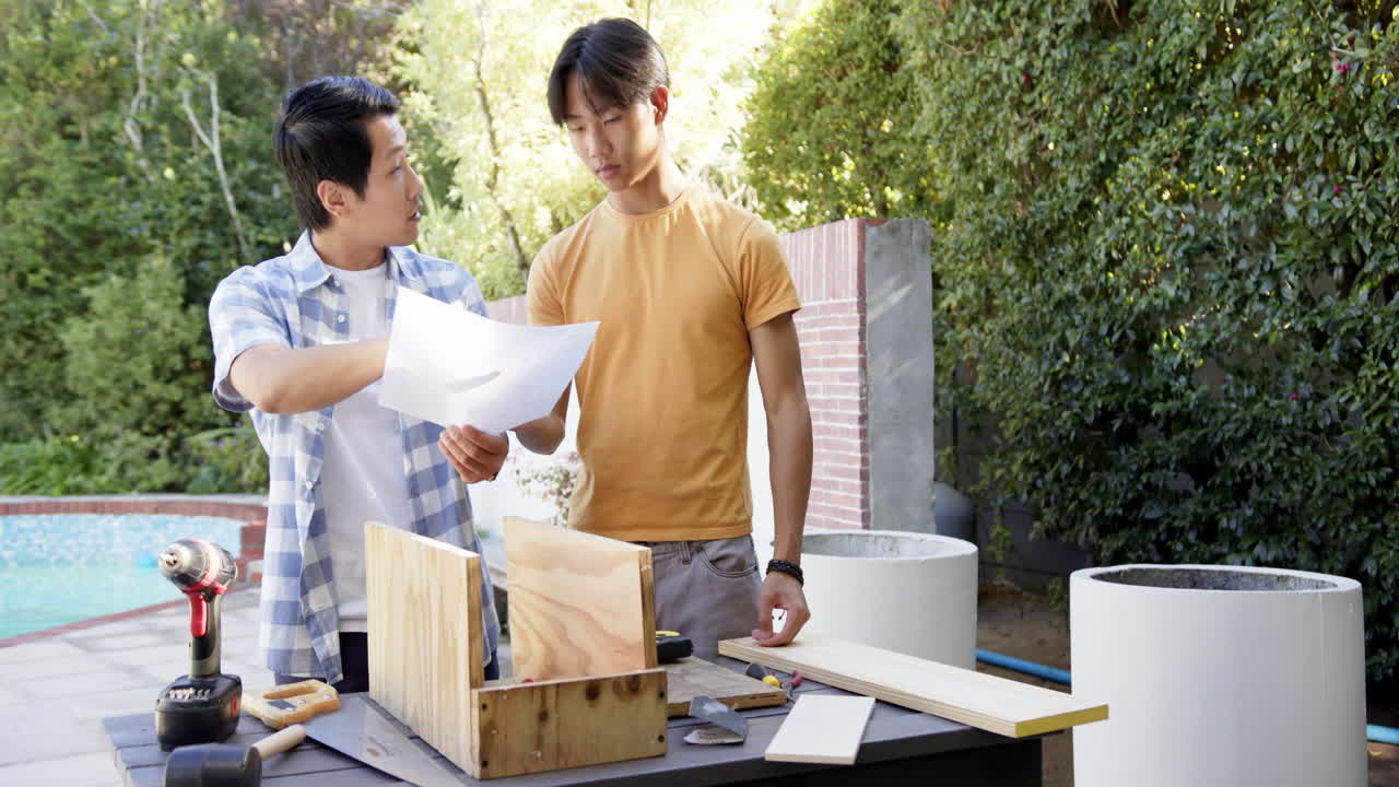 Asian father and son working on woodworking project together outdoors