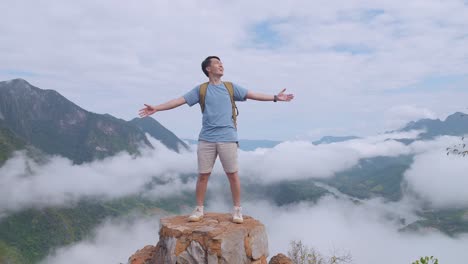 asian hiker male standing on the rock and raising his hands celebrating reaching up top of foggy mountain