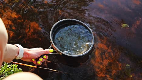 grease and river swirl in slow motion as pan is dipped and cleaned outdoors