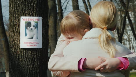 mom soothes the girl who lost the dog on the tree hangs the announcement of the missing puppy