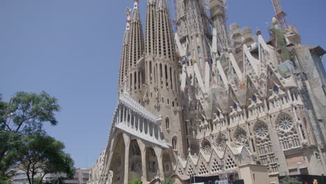 Vista-Del-Cielo-A-Través-De-árboles-Ventosos-Mientras-Pasan-Los-Vehículos,-La-Famosa-Catedral-De-La-Sagrada-Familia-En-Barcelona,-España,-Temprano-En-La-Mañana-En-6k