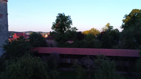 a-drone-flies-through-the-park-to-a-covered-footbridge-passing-a-tower-in-the-city-wall