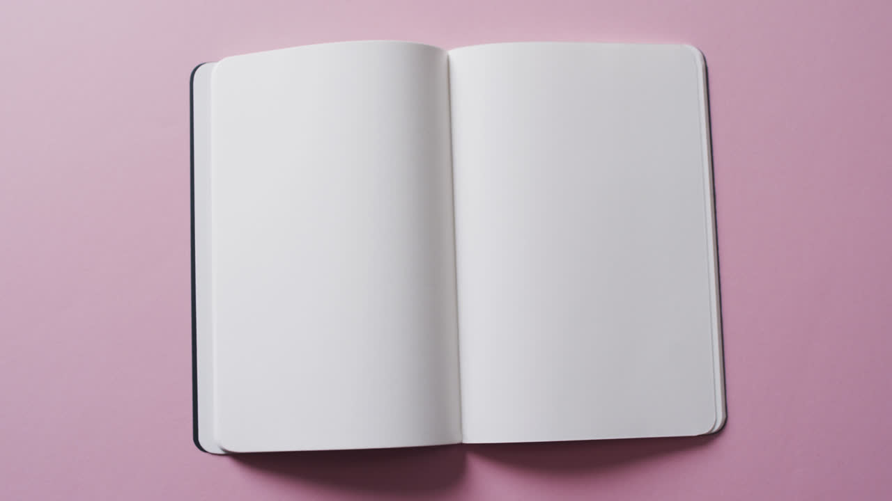 Close up of open blank book with copy space on pink background in slow motion