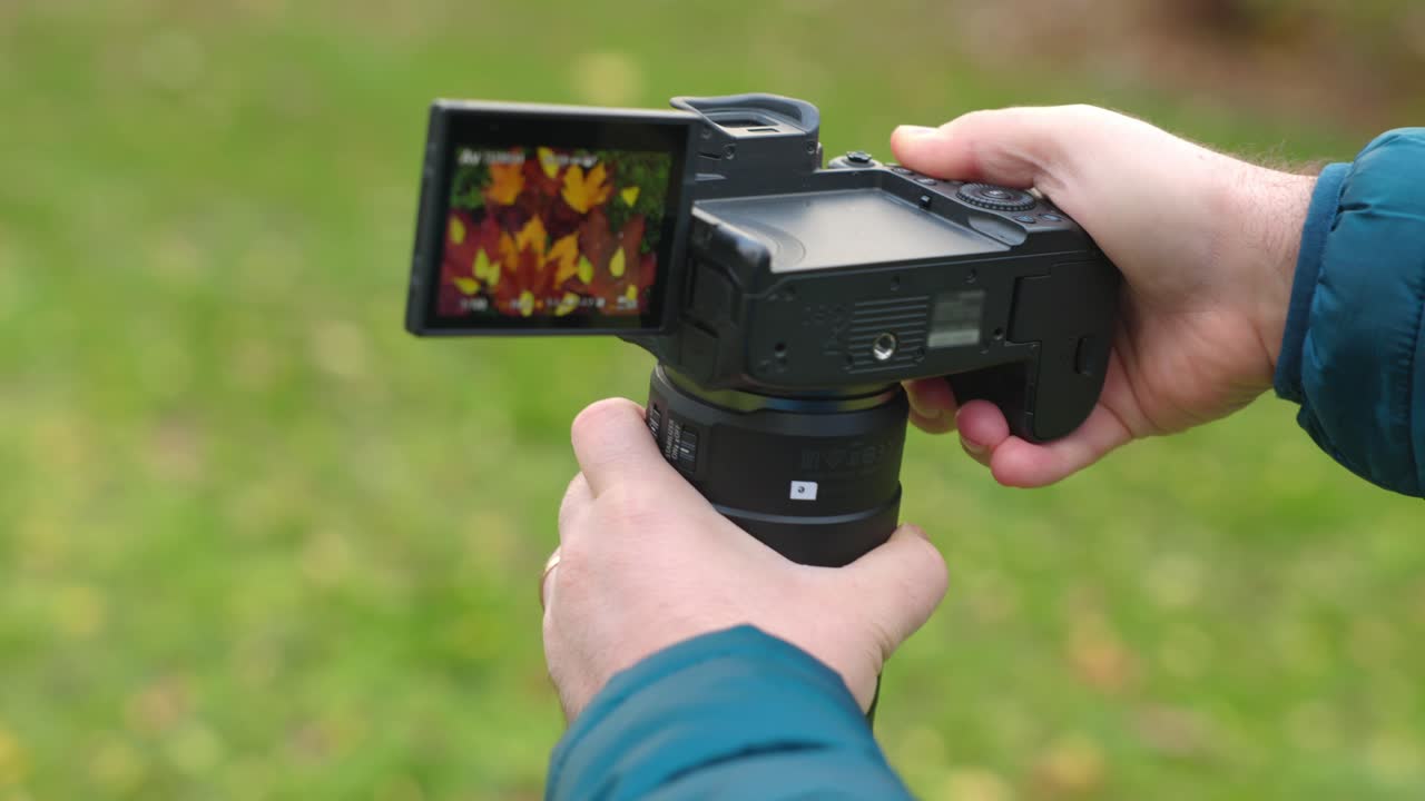 Mand i parken tager et foto med et afstandsmålerkamera og folder derefter skærmen tilbage